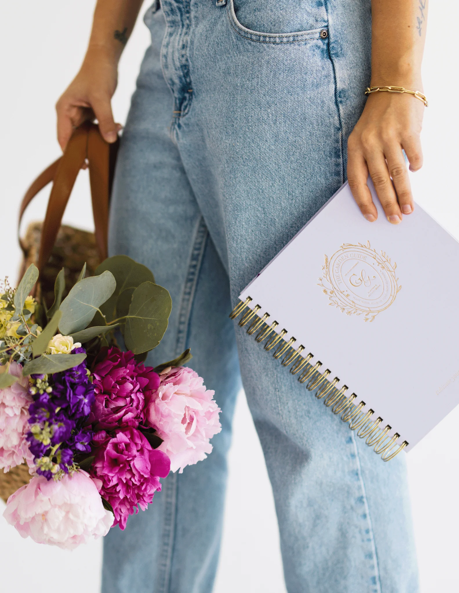 Woman in jeans holding a Floriss Garden Guide planner and a basket of pink and purple flowers, welcoming neurodivergent women into the Floriss community